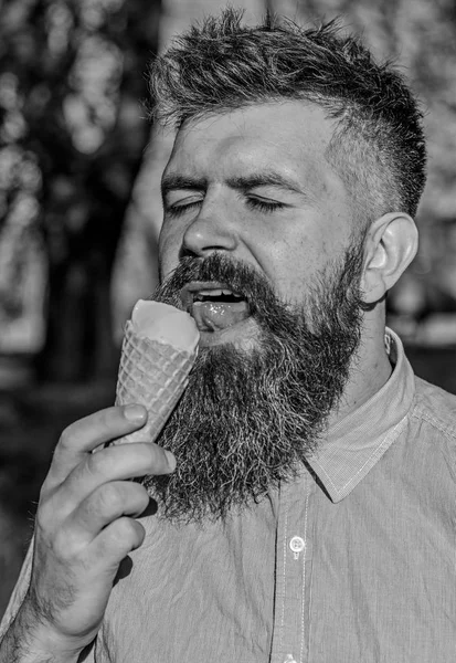 Skrämmande koncept. Mannen med skägg och mustasch på lugna ansikte-äter glass, natur bakgrund, oskärpa. Man med långt skägg kylning med glasstrut solig varm dag, närbild — Stockfoto