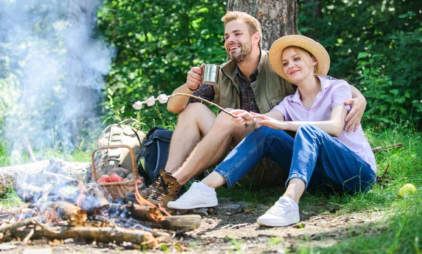 Roasting marshmallows at bonfire. Hike picnic. Couple eat snacks and drink. Couple friends prepare roasted marshmallows snack nature background. Couple in love camping forest roasting marshmallows
