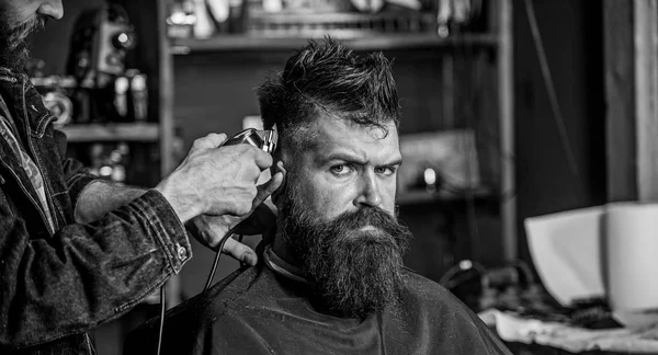 Stylish haircut concept. Hands of barber with clipper close up. Client with beard on salon background. Hipster bearded client on strict face getting hairstyle. Barbers hand with hair clipper trimming — Stock Photo, Image