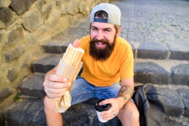 Senin yemek kavramı tadını çıkarın. Sakallı adam hipster sokak gıda kentsel arka plan tadını çıkarın. Kent gıda kültür kavramı. Hipster merdivenlerde açık havada sit süre sosisli sandviç ye. Lezzetli sosisli sandviç sosis roasty topuz