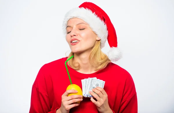 女孩圣诞老人帽子喝果汁柠檬同时持有桩钱。用新鲜柠檬汁赚钱。圣诞利润概念。柠檬钱的概念。财富和丰富的象征。富有的女孩柠檬和钱 — 图库照片