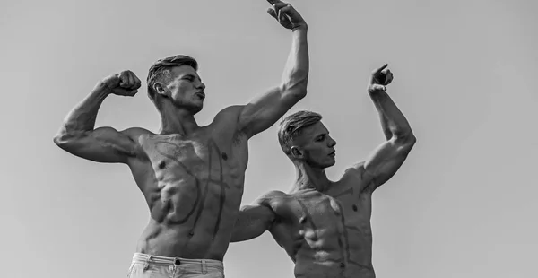 Homens musculosos com tronco sexy nu, céu no fundo. Atletas com venda de inscrição em baús musculares. Atletas em faces sérias demonstrando força e poder de seus músculos. Conceito de vendas — Fotografia de Stock