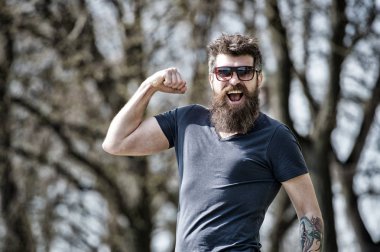 Kendine güvenen sakal bakışla maço acımasız güneş gözlüğü. Adam kas kol gücü jest sakallı. Adam hipster giyim güneş gözlüğü doğa arka plan sakallı. Sakal erkeklik özniteliği. Erkeklik kavramı