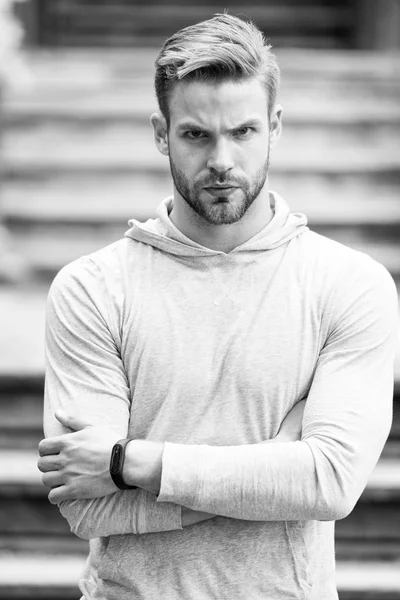 Beau dans le style. Homme bras croisés non rasés semble beau et cool. Guy barbu attrayant se soucie de l'apparence. Homme soies visage sérieux, fond urbain, déconcentré. Concept métrosexuel — Photo