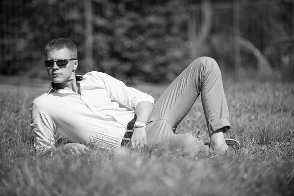 Empresario en gafas de sol en sol al aire libre. El hombre se relaja sobre hierba verde. macho guapo disfrutar del día de verano. Estilo y tendencia de moda. Concepto de tiempo de descanso — Foto de Stock