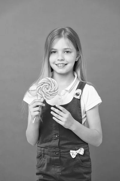 Prova min lollipop litet barn leende med godis pinne på lila bakgrund. Flickan ler med lollipop på lila bakgrund. Lycklig unge med swirl karamell. Mat och efterrätt. Diet och bantning — Stockfoto