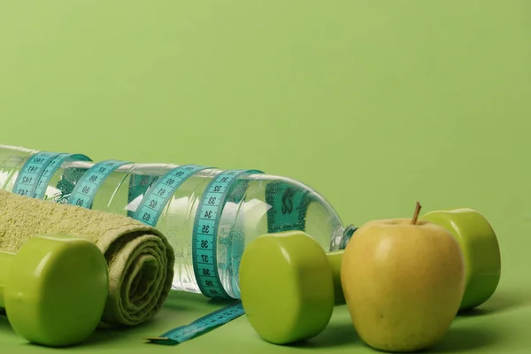 Dumbbells in green color, water bottle, measure tape, towel, fruit