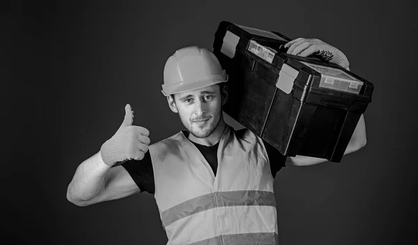Mann mit Helm, Hut hält Werkzeugkiste und zeigt Daumen hoch Geste, blauer Hintergrund. Arbeiter, Reparateur, Reparateur, Bauarbeiter auf selbstbewusstem Gesicht trägt Werkzeugkiste auf der Schulter. Reparaturberatungskonzept — Stockfoto
