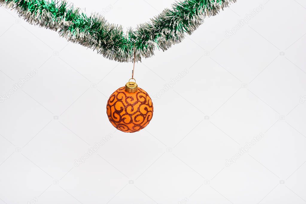 Tinsel with pinned christmas toy, white background, copy space. Christmas ornament concept. Ball with glamorous ornaments hang on shimmering green tinsel. Decoration for Christmas tree hang on tinsel