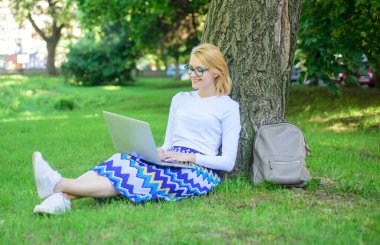Kız oturup ot yalın ağaç gövdesi ile defter. Wi fi ağ bağlantısı ücretsiz erişim. Bayan, serbest meslek sahibi Park'ta çalışma. Kadın dizüstü işleri açık, park arka plan ile. Serbest avantajları taking