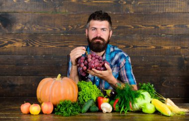 Tarım ve kavram hasat. Sakallı adam üzüm ahşap arka plan tutar. Çiftçi masada homegrown hasat ile. Sebze organik hasat. Çiftçi hasat sebzeler ve üzüm gurur
