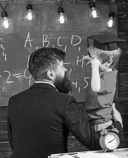 在毕业帽的孩子讨论黑板上的涂鸦 而老师听 神童儿童概念 老师带着胡子 父亲在教室里教小儿子 黑板上的背景 — 图库照片