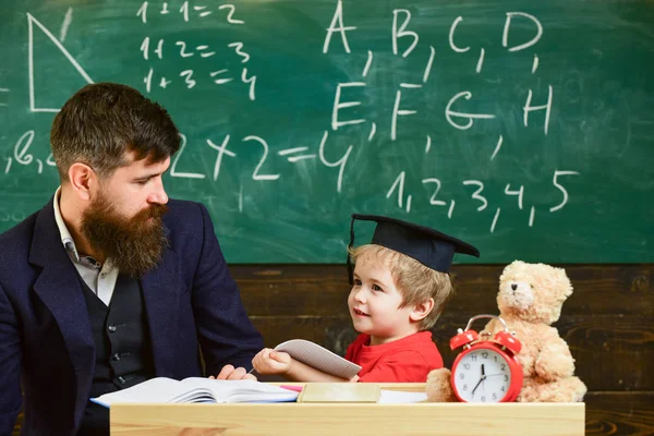 Öğretmen ve öğrenci kolej, kara tahta arka plan içinde. Çocuk mutlu çalışmalar öğretmen, evde ile ayrı ayrı. Bireysel eğitim kavramı. Evlat, küçük çocuk öğretmen öğretir sakal, baba