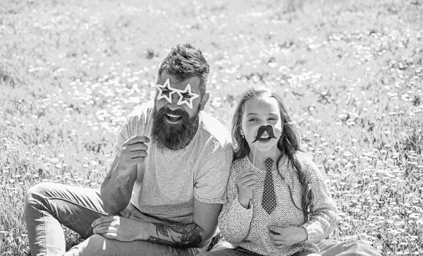 Conceito dos melhores amigos. O pai e a filha sentam-se na relva no campo, fundo verde. Família passar o lazer ao ar livre. Criança e pai posando com óculos, bigode e amarrar atributos de cabine de fotos — Fotografia de Stock