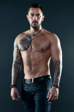 Kas dövmeli atlet göz çekici. Spor ve moda kavramı. Dövme ile kot giyiyor poz uygun yakışıklı. Dövme sanatı. Yakışıklı adam gömleksiz koyu arka plan üzerinde kot ile kas