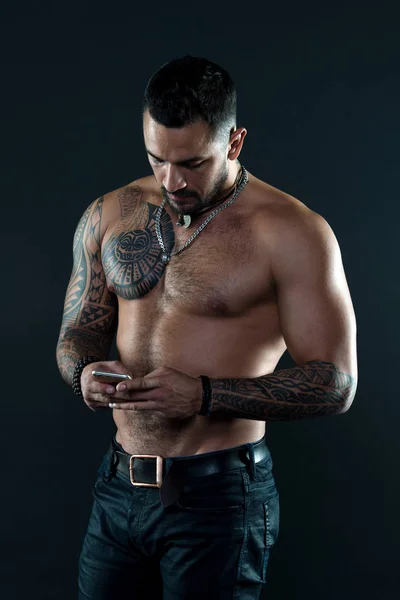 Надіслати повідомлення. Красива відповідна людина відправляє повідомлення смартфона. М'язистий татуйований спортсмен виглядає привабливо. Концепція обміну повідомленнями. Чоловік красивий без сорочки м'язистий з джинсами на темному тлі — стокове фото