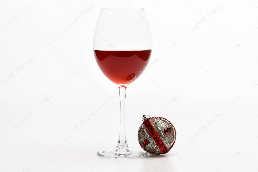 Wineglass with red liquid or wine and christmas ball ornament isolated on white background. Winter celebration with alcohol drink. Winter holidays concept. Glass with wine and christmas decoration