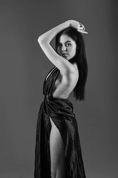 Lady, sexy girl in dress. Fashion and vogue concept. Woman in elegant black long evening dress with nude back, dark background. Attractive pensive girl wears fashionable dress with erotic slit on hip — Stock Photo, Image