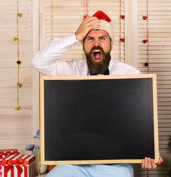 Santa Claus in hat with troubled face. Guy with chalkboard