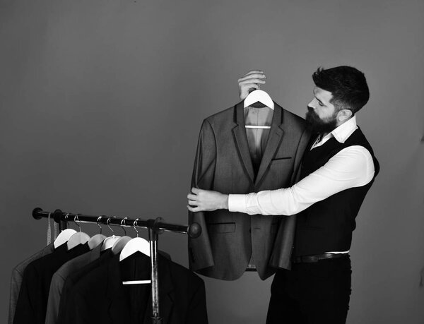 Продавец держит серый костюм на вешалке.