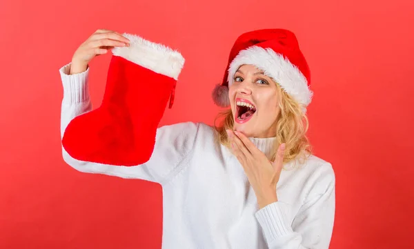 Traditioneller Winterurlaub. Inhalt von Weihnachtsstrumpf prüfen. Frau mit Weihnachtsmütze halten Weihnachtsgeschenk roten Hintergrund. Mädchen fröhliches Gesicht bekam Geschenk in Weihnachtssocke. Weihnachtsstrumpfkonzept — Stockfoto