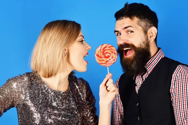 Жінка і бородатий чоловік їдять льодяник на синьому фоні — стокове фото