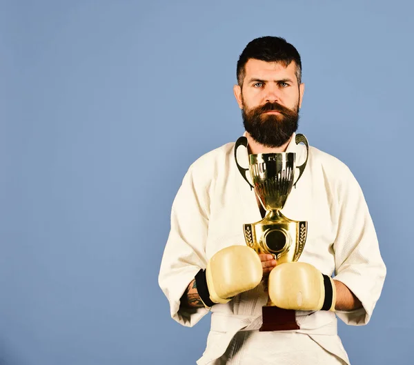 Karate man with serious face in boxing gloves holds cup