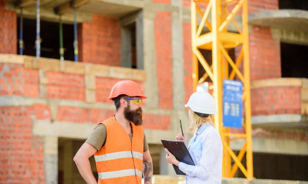 Discuss progress project. Safety inspector concept. Woman inspector and bearded brutal builder discuss construction progress. Construction project inspecting. Construction site safety inspection