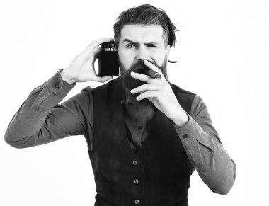 Sakallı adam puro içiyor, ciddi bir yüzü var, parfüm tutuyor.