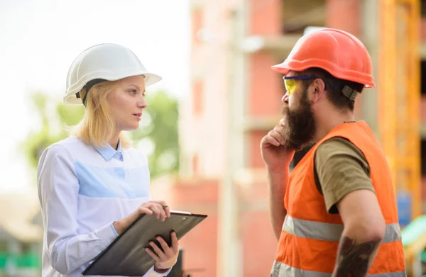 Diskutera framsteg projekt. Bygg projekt inspekterar. Inspektör säkerhetskoncept. Kvinna inspektör och skäggiga brutala builder diskutera byggandet framsteg. Konstruktionsbesiktning webbplats säkerhet — Stockfoto