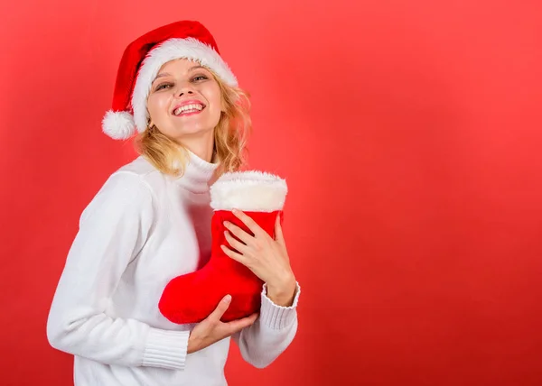Tradiční Zimní dovolená. Zkontrolujte obsah šlapku. Žena v santa hat držet vánoční dárek červené pozadí. Vánoční punčocha koncept. Dívka Veselý obličej dostal dárek vánoční ponožka — Stock fotografie