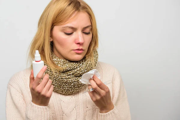 Girl in scarf hold nasal spray and tissue. Cold and flu remedies. Runny nose and other symptoms of cold. Nasal drops bottle. Nasal spray runny nose remedy. Woman feels badly ill sneezing