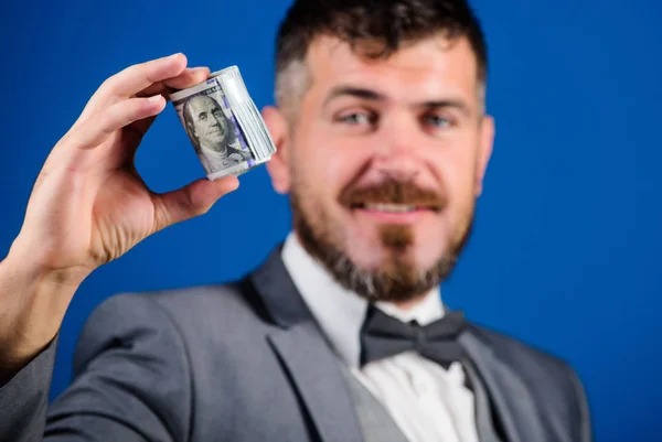 Man bearded hipster hold rolled dollars banknotes. Guy formal suit offer bribe or purchase. Easy money concept. Rich businessman hold rolled money. Hipster offer money blue background close up