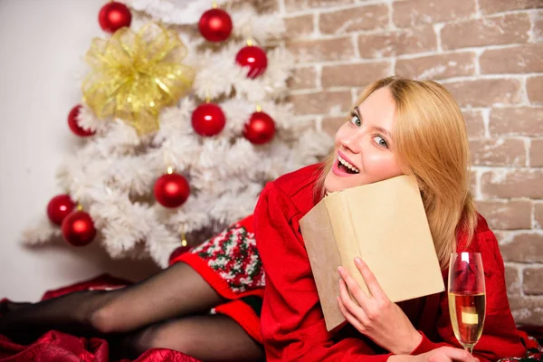 Woman hold glass champagne and book. Girl relax near christmas tree. Lady celebrate christmas alone. Winter holidays concept. Waiting for christmas. Girl wear red dress sit near christmas tree — Stockfoto