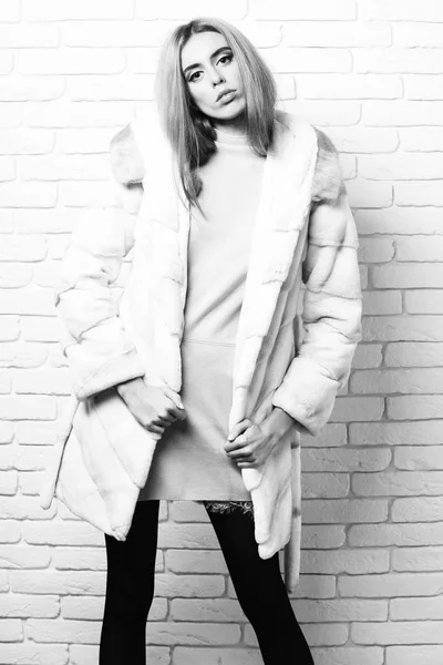 Junge modische sexy hübsche Frau oder Mädchen mit schönen langen blonden Haaren in Taille Mantel aus weißem Fell mit rosa Kleid und Mode-Make-up auf Backstein Wand Studio Hintergrund — Stockfoto