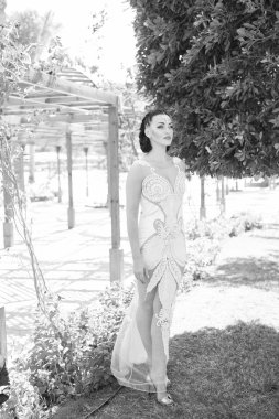 Harika görünüyorsun. Saç makyaj kadın nakış ve inciler ile moda sıkı uygun elbise giyer. Bayan lüks kıyafeti egzotik bahçe arka plan yürür. Kız çekici seksi pahalı elbise görünüyor