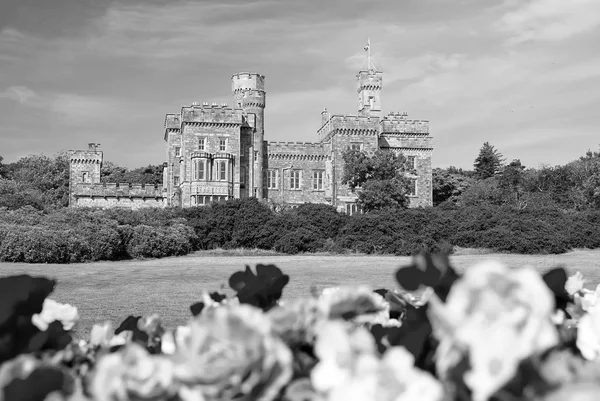 Lews Castle in Stornoway, United Kingdom with blurred roses in foreground. Castle with green grounds on blue sky. Historic architecture and design. Landmark and attraction. Summer vacation on isle