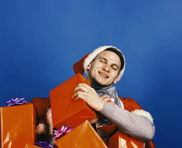 Chico con cara feliz tiene muchos regalos rojos y plateados. — Foto de Stock