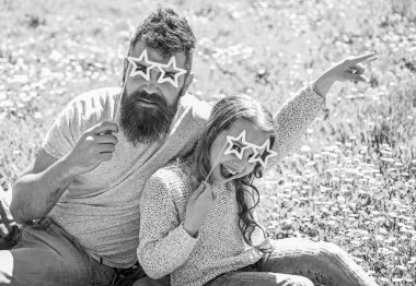 Rock yıldız kavramı. Aile açık havada eğlence harcamak. Baba ve kızı, grassplot, arka planı yeşil çimenlerin üzerinde oturur. Çocuk ve yıldız şekilli eyeglases photo booth özniteliğine çayır ile poz baba