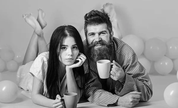 Pár reggel kávéval lazítson. Férfi és nő a mosolygó arcok feküdt, rózsaszín háttér. Hétvégén reggel koncepció. A pár a szerelem kávét iszik az ágyban. Férfi és nő a hazai ruházat, pizsama — Stock Fotó