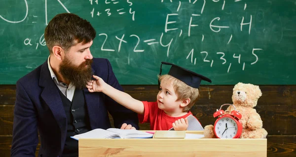 Lärare och elev i mortarboard, svarta tavlan på bakgrund. Kid glada distrahera medan du studerar, uppmärksamhetsstörning. Stygga barn koncept. Far med skägg, lärare lär son, liten pojke — Stockfoto