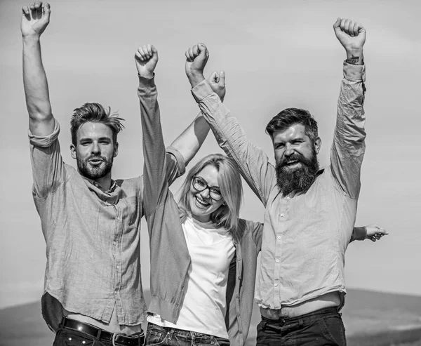 Company reached top. Company of three happy colleagues or partners celebrating success, sky background. Success concept. Men with beard in formal shirts and blonde in eyeglasses as successful team