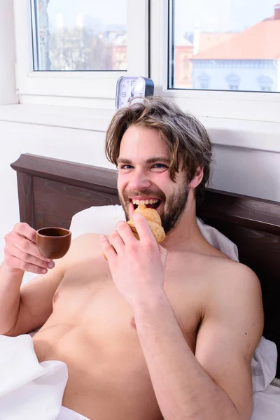 Французький сніданок стереотип. Хлопець маючи кава і утримань круасан під час лежав ліжка в спальні номер або hotel. Людина бородатий красивий хлопець їжі сніданок в ліжко. Людина їсть круасани і пити каву — стокове фото