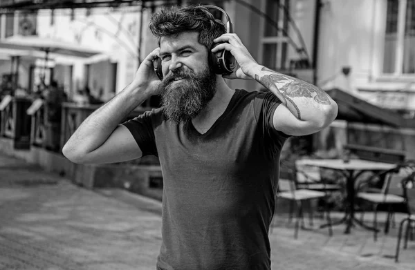 Homem com barba comprida e bigode com auscultadores sem fios na cabeça, fundo urbano desfocado. Hipster com fones de ouvido no rosto sorridente ouvir música enquanto caminha. Conceito de tecnologias sem fio — Fotografia de Stock