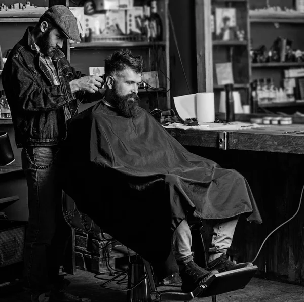 Peluquero con cortapelos trabaja en el corte de pelo de barbudo chico fondo de la barbería. Hipster cliente cortarse el pelo. Peluquero con cortador de pelo recortado en la nuca del cliente. Hipster concepto de peinado — Foto de Stock