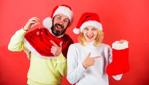 Verifique o conteúdo do presente de meia de Natal recebido. Conceito de presente de Natal. Casal cara alegre confira presente na meia de Natal. Mulher e homem barbudo em santa chapéu esperando presente vermelho fundo — Fotografia de Stock