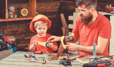 Babalık kavramı. Çocuk, çocuk ile baba el testeresi kullanmayı öğrenme koruyucu kask içinde meşgul. Baba, anne-baba ile oğlu oyuncakla oynarken testere için küçük oğlu öğretim sakal gördüm