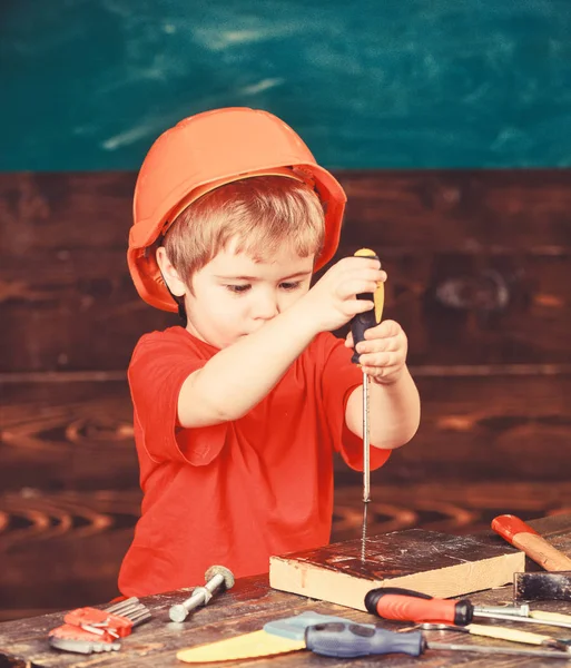 Junge hält Schraubenzieher in der Hand. Kleinkind auf geschäftigem Gesicht spielt in Werkstatt mit Schraubenzieher Kind mit Helm niedlich spielen als Bauarbeiter oder Reparateur, oder basteln. Bastel- und Werkstattkonzept — Stockfoto