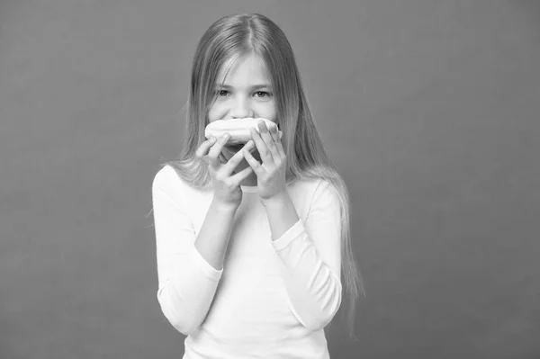 A comer qualquer coisa. A criança come donut no fundo violeta. Menina com donut anel envidraçado no fundo roxo. Um miúdo com comida de plástico. Comida para lanche e sobremesa. Infância e puericultura, espaço de cópia — Fotografia de Stock