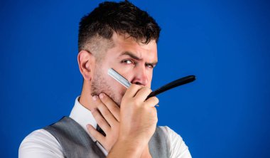 Kuaför keskin tehlike ustura ile tıraşsız hippi. Berber Kuaför Salonu. İpuçları bakım Kuaför sakal. Erkek yelek papyon ile usturanın mavi arka plan tutun. Kuaför sanat kavramı